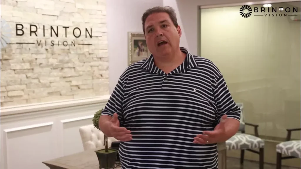 Bernie testimonial; Bernie is a tall, fat white man with brown hair wearing a striped shirt. He stands in the Brinton Vision office and has his mouth open as he talks. His hands are in front of him in a gesture to emphasize what he's saying